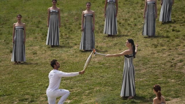 Actress Mary Mina, playing high priestess, gives the flame to the first torch bearer, Greek olympic gold medalist Stefanos Douskos during the official ceremony of the flame lighting for the Paris Olympics, at the Ancient Olympia site, Greece, Tuesday, April 16, 2024. The flame will be carried through Greece for 11 days before being handed over to Paris organizers on April 26. (AP Photo/Petros Giannakouris)